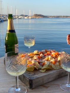 a table with wine glasses and a pizza on it next to the water in front of some boats