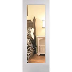 a mirror reflecting a bed and nightstand in a room with white walls, wood floors and flooring