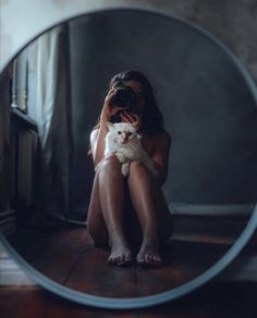 a woman is holding a cat and taking a photo in the mirror with her camera