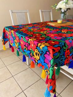 a colorful table cloth with flowers and tassels on it sits in front of a white bench