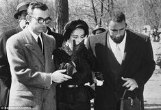 black and white photograph of men in suits looking at something on the ground with trees behind them