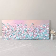 a pink and blue painting on a wall next to a vase with flowers in it