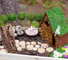 a miniature garden in a wooden box filled with rocks and grass, including a small house