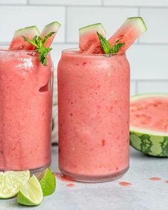 two glasses filled with watermelon smoothie next to sliced cucumbers and limes