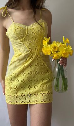 a woman in a short yellow dress holding a vase with flowers on the side and wearing sunglasses