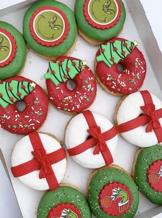 twelve decorated christmas donuts in a box with red ribbon and green sprinkles