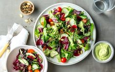 two white bowls filled with salad on top of a metal table next to silverware