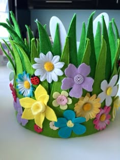 a green felt crown with flowers and ladybugs on the front is sitting on a table