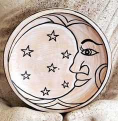 a wooden plate with a drawing of a moon and stars on the face, sitting on top of some rocks