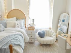 a bedroom decorated in white and blue with lights on the window sill, chair, bed, desk and mirror