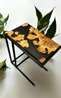 a black and gold side table sitting next to some green leafy plants on a white surface