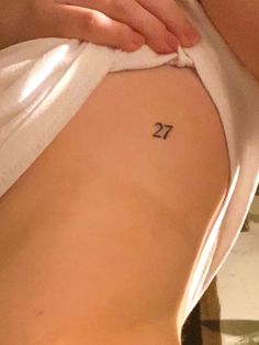 a woman's lower back tattoo with the number twenty seven on her left side