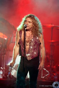 a man with long hair standing in front of a microphone on stage at a concert