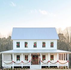 a white house decorated for christmas with wreaths on the front porch and red ribbon around the windows