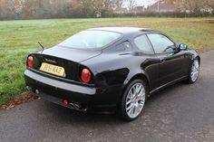 a black sports car is parked on the side of the road in front of some grass