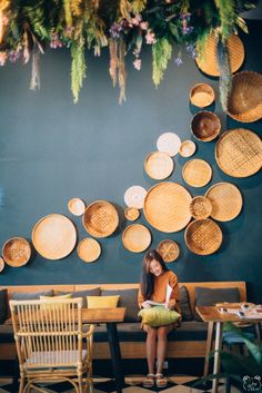 a woman sitting on a bench in front of a wall with baskets hanging from it