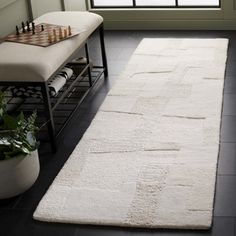 a large white rug in front of a window next to a bench and chess board