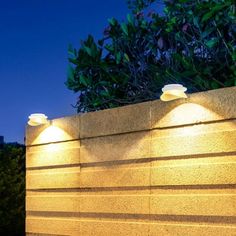 three lights on the side of a wall next to trees and bushes at night time