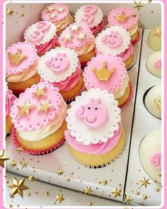 cupcakes with pink frosting and gold stars are in a box on the table