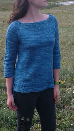 a woman standing in the grass wearing a blue sweater