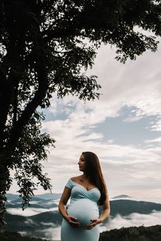 a pregnant woman standing under a tree with her hands on her hips and looking at the sky