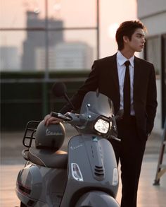 a man in a suit and tie standing next to a scooter