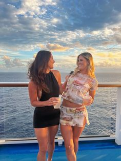 two beautiful women standing next to each other near the ocean on a cruise ship at sunset