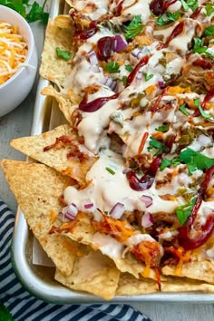 nachos with meat, cheese and sauce in a pan next to a bowl of shredded cheese