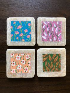 four square coasters with different designs on them sitting on a wooden table, each decorated with flowers and leaves