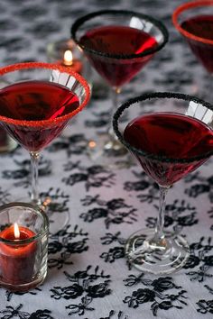 three glasses filled with red liquid sitting on top of a table next to a candle