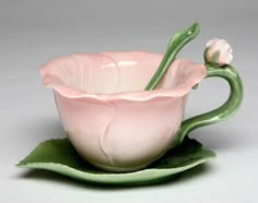 a pink flower sitting inside of a cup on top of a green saucer