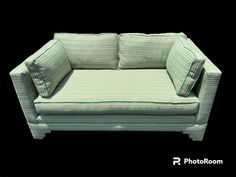 a green and white couch with two pillows on it's back end, sitting in front of a black background