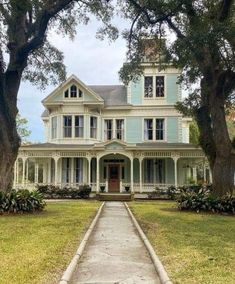 a large blue house sitting on top of a lush green field next to tall trees