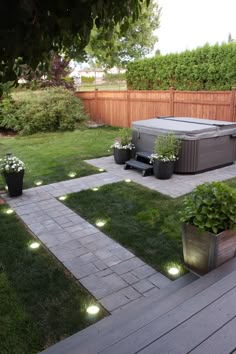 a hot tub sitting in the middle of a yard next to a wooden deck with potted plants