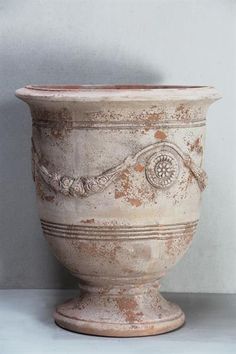 an old white vase sitting on top of a table next to a gray wall and floor