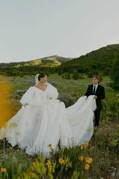 a bride and groom walking through the grass in an open field with wildflowers