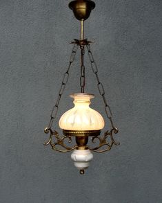 an old fashioned chandelier hanging from a chain on a gray wall with a white glass shade