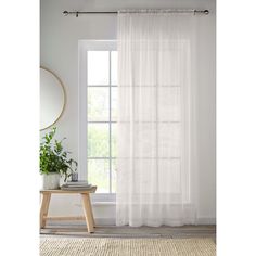 a white curtain hanging on the side of a window next to a table with a potted plant