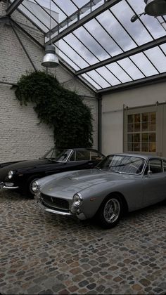 two classic cars parked in front of a white brick building with glass roof and windows