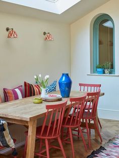 a dining room table with red chairs and blue vases on top of it in front of a window