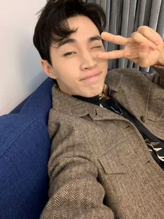 a young man sitting on a couch making the peace sign with his hand while wearing a suit and tie