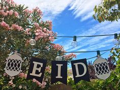 the letters eid are hung on clothes pins in front of some flowers and trees