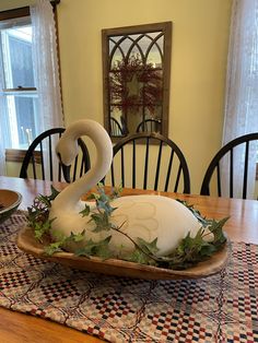 a swan sculpture sitting on top of a wooden table next to a bowl filled with leaves