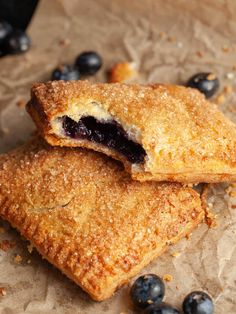 two blueberry pastries sitting on top of wax paper next to some blueberries