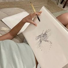 a woman laying on the floor with a drawing board and pencils in her hand