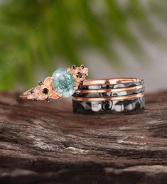 three rings with different colored stones on top of a wooden surface and green leaves in the background