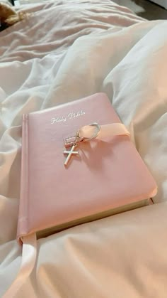 a pink book with a cross on it laying on a bed covered in white sheets