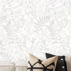 a white couch with two pillows on it and a wallpaper behind the couch is a plant pattern