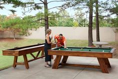 two people are playing pool in the back yard, while one person is leaning over to check out the bill table