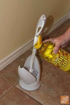 a person is holding a bottle in front of a toothbrush holder on the floor